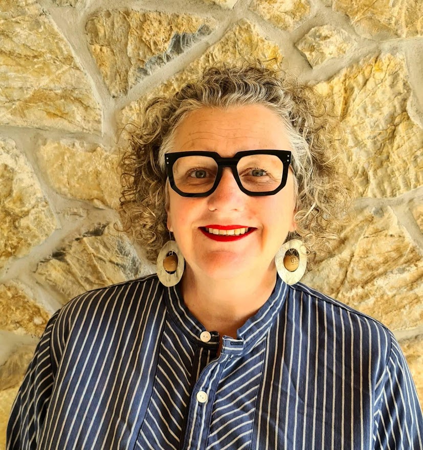 Woman with curly hair and glasses smiling against stone wall background